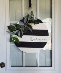 a black and white striped wreath hanging on a door with the word welcome painted on it