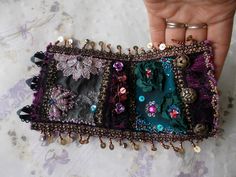 a woman's hand is holding a small purse with buttons and beads on it