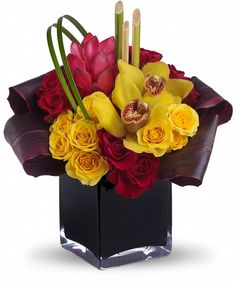 a square vase filled with yellow and red flowers on top of a white background,