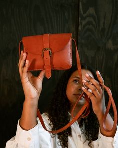 "Bouk" means buckle in Creole. This cute styled bag has a center buckle. This cute lightweight bag with high end style is great when you're on the go. Handcrafted in Haiti 100% Vegetable-tanned leather Available in three colors; Dark, Black and Cognac Stamped with Haiti Made logo 7"L x 4"W x 5"H This is a handmade leather item, so there will be variations in color and markings, adding to the unique character of the product. For reference: Model pictured in tan is 5'4" tall and model pictured in Lightweight Bag, Small Crossbody Bag, Small Crossbody, Model Pictures, Leather Items, Three Color, Vegetable Tanned Leather, Handmade Leather, Haiti