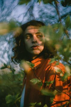 a man standing in front of some trees with his eyes closed and looking at the camera