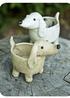 two small ceramic dogs sitting on top of a tree stump in front of each other