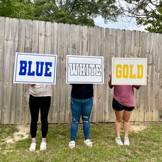 three women holding signs that say blue, white and gold in front of a fence