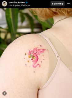 the back of a woman's shoulder with a pink dragon tattoo on her left side