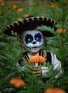 a young boy with blue and white face paint holding an orange flower in his hand