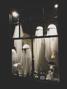 three mannequins dressed in white are seen through a window