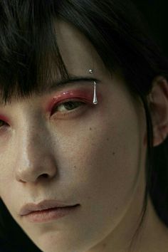 a close up of a person with eye makeup and piercings on their forehead, looking at the camera