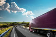 a semi truck driving down the road in front of a blue sky with white clouds