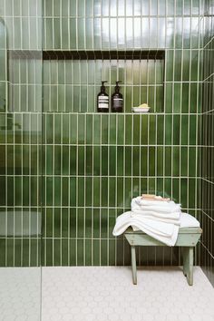 a white towel sitting on top of a wooden bench in front of a green tiled shower