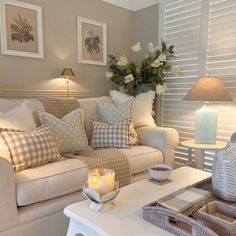 a living room filled with furniture and flowers on top of a white coffee table in front of a window