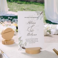 a welcome card on a wooden stand next to a table with silverware and flowers