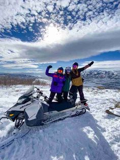 two people standing on top of a snowmobile in the snow with their arms up