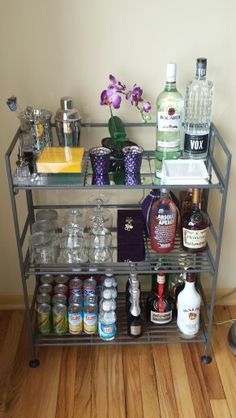 a metal shelf filled with bottles and glasses on top of a hard wood floor next to a wall