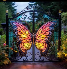 an iron gate with a stained glass butterfly on it's side and flowers in the background