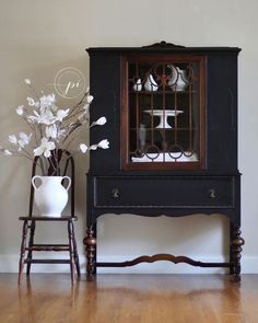 a vase with white flowers sitting on top of a wooden table next to a black cabinet