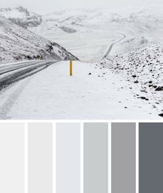 a snowy road with mountains in the background and a yellow post at the end that is surrounded by snow