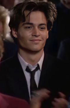 a close up of a person wearing a suit and tie with other people in the background