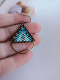 a hand holding a small triangle shaped beaded ring