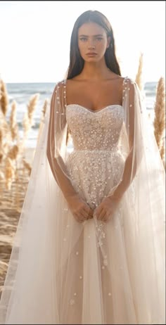 a woman in a wedding dress standing on the beach with her arms behind her back