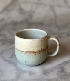 a white and brown cup sitting on top of a marble counter next to a wall