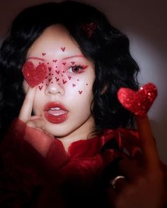 a woman with red makeup and hearts on her face is holding two fingers up to her face