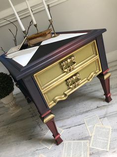 an old dresser is painted gold and purple with some white candles in the corner next to it