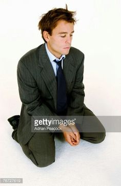 a man in a suit and tie sitting on the floor with his hands folded up