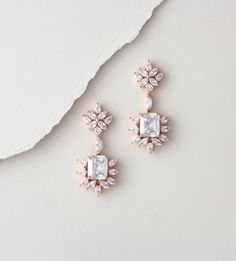 two pairs of diamond and pearl earrings on a white surface with a piece of paper in the background