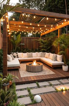 an outdoor living area with wooden decking and lights strung over the fire pit, surrounded by greenery