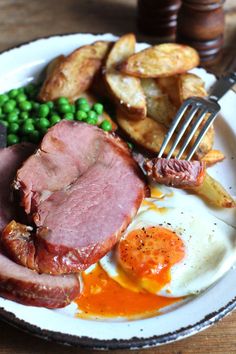 a white plate topped with meat, potatoes and peas next to a knife and fork