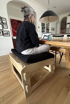 an older woman sitting at a wooden table with a laptop computer on top of it