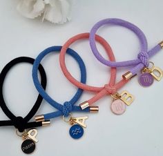 four different colored bracelets with gold charms on one side and an initial charm on the other