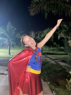 a woman in a red cape and blue shirt is standing on the sidewalk with her arms outstretched