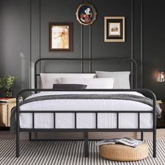 a black metal bed frame with white sheets and pillows in a dark room, along with pictures on the wall