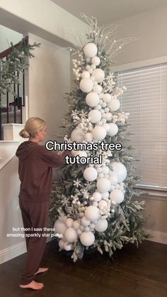 a woman is decorating a christmas tree with white balls and silver baubies