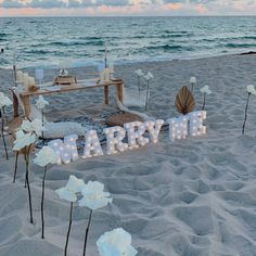 a sign that says marry me on the beach with flowers in front of it and an ocean view