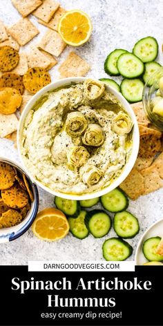 a bowl of spinach artichoke hummus surrounded by cucumbers and crackers