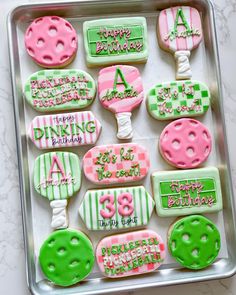 birthday cookies decorated with pink, green and white icing are in a metal tray