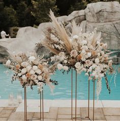 three gold vases with flowers and feathers in front of a swimming pool at a wedding