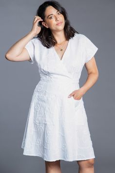 a woman in a white dress posing for the camera with her hands on her head