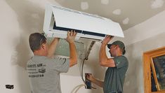 two men working on an air conditioner in a room that is being remodeled and painted