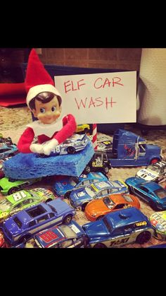 an elf sitting on top of a pile of toy cars next to a sign that says elf car wash