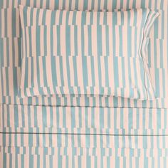 a bed with blue and white striped sheets on top of it, next to a pillow