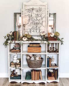 a book shelf with books, candles and other items on it in front of a white wall