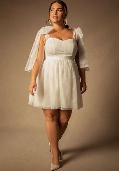 a woman in a short white dress with a veil on her head and heels, posing for the camera