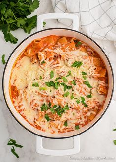 a pot filled with pasta and sauce on top of a white counter next to parsley