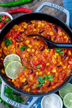 a skillet filled with chili and corn on top of a cutting board next to limes