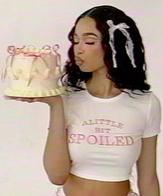 a woman holding a cake in her right hand and wearing a white shirt with the words'believe best spoiled'on it