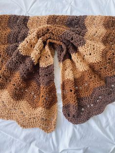 a crocheted scarf laying on top of a white sheet covered in brown and tan colors