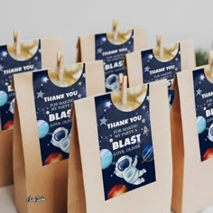 small brown bags with space themed thank you tags on them are sitting on a table